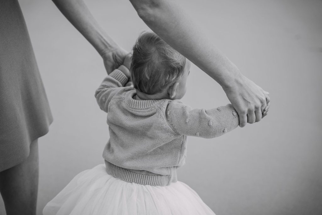 Adults holding a baby's hands, helping her walk.