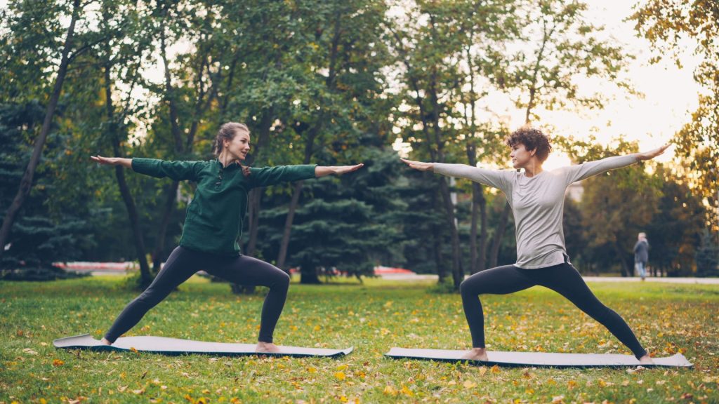 Two women practicing yoga in a park.